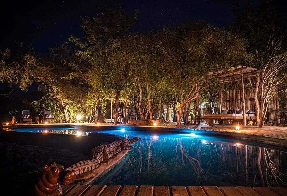 Lit pool and thatched decks glow beneath the trees at Changa Safari Camp, Matusadona.
