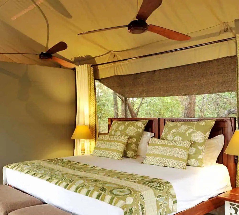 Twin ceiling fans turn above a garden-view bed inside a tent at Changa Safari Camp.