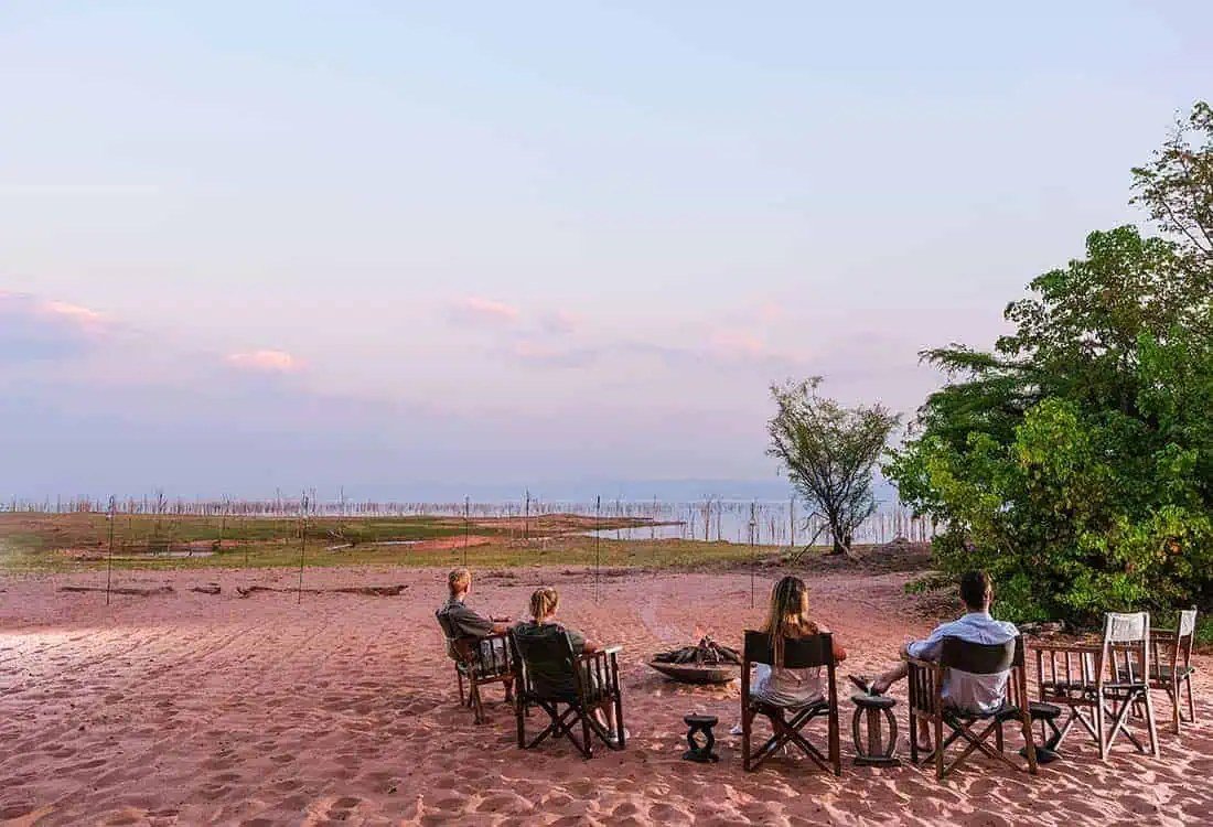 Guests gather in camp chairs on Lake Kariba's shore at Changa Safari Camp at dusk.