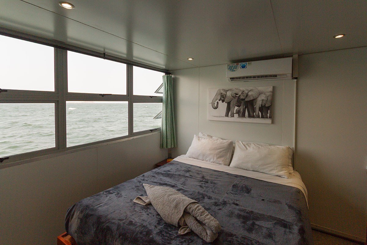 Elephant print above a double bed with lake views through cabin windows aboard Malachite.
