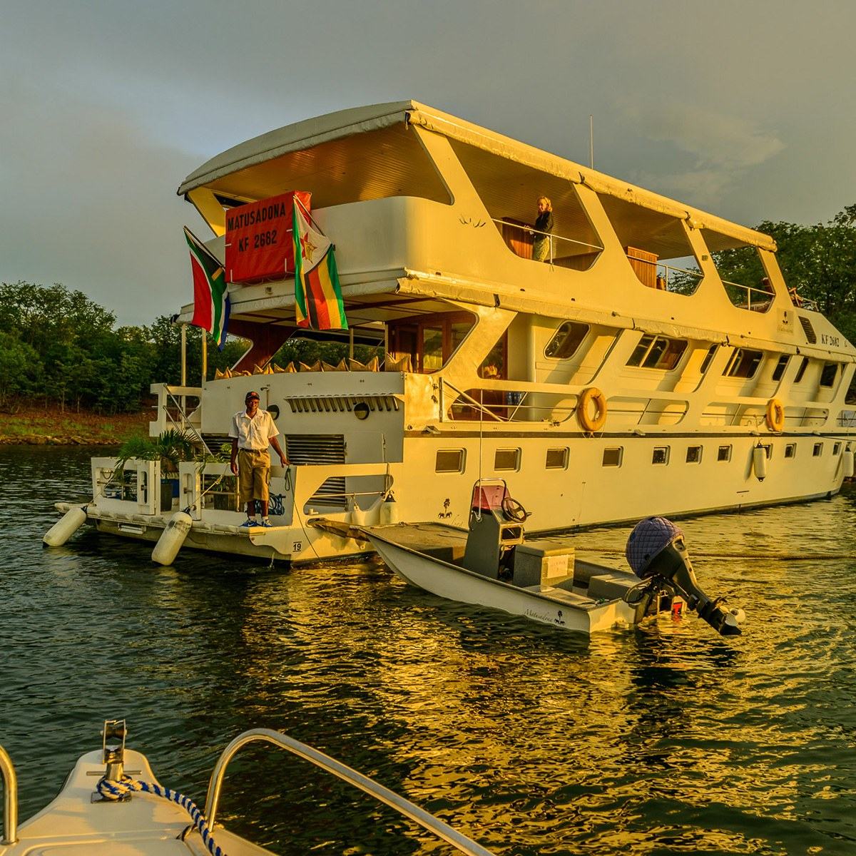 The houseboat MV Matusadona moored at golden hour with a crew member on deck.