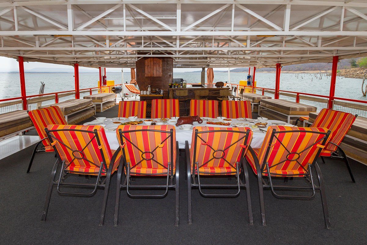 Open-air dining deck set for a meal with lake views aboard Peregrine houseboat.